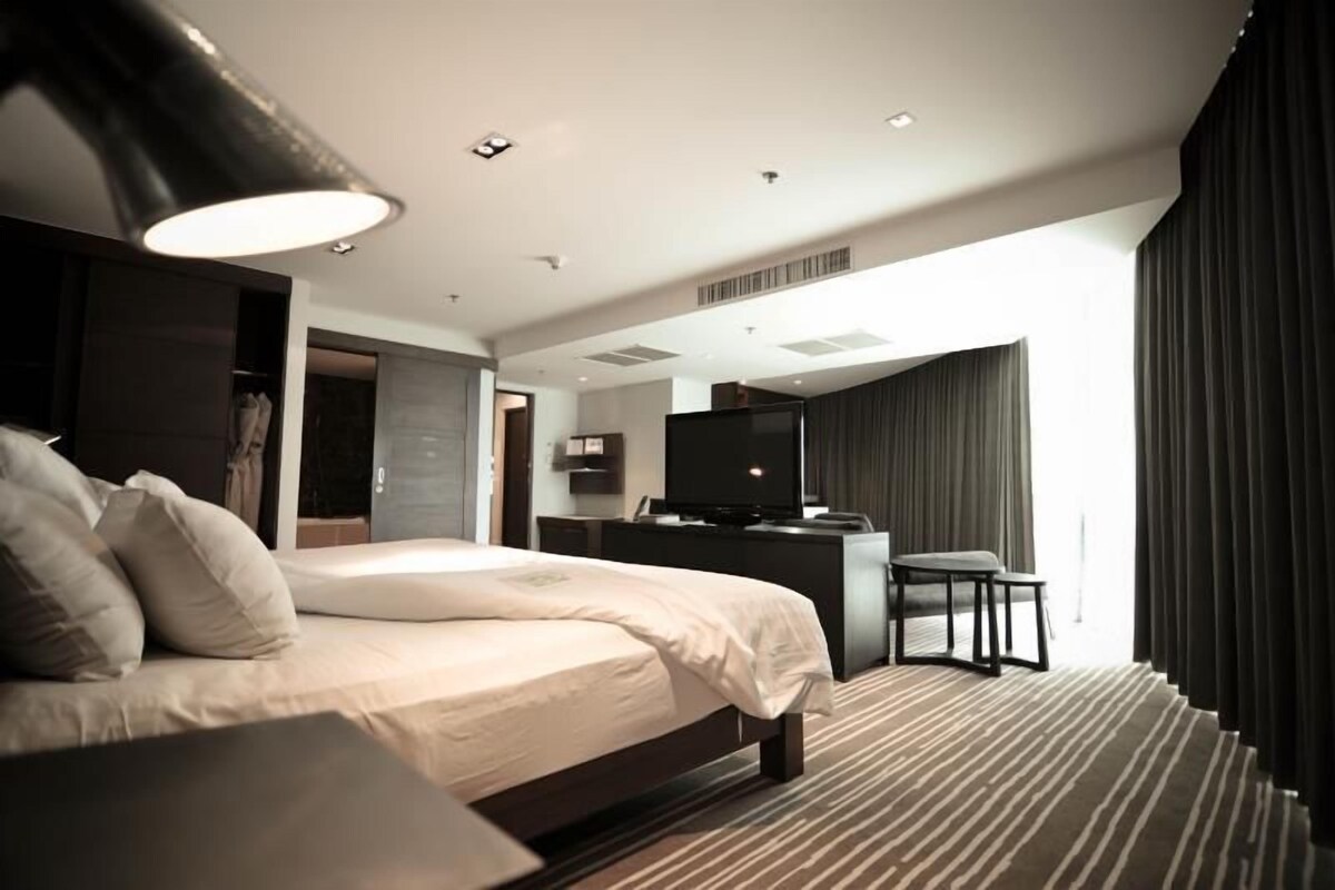 A modern hotel room with a large bed, a desk, a television, and a view of the city.