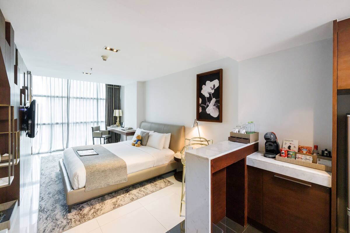 A modern hotel room with a large bed, a desk, a chair, and a view of the city.