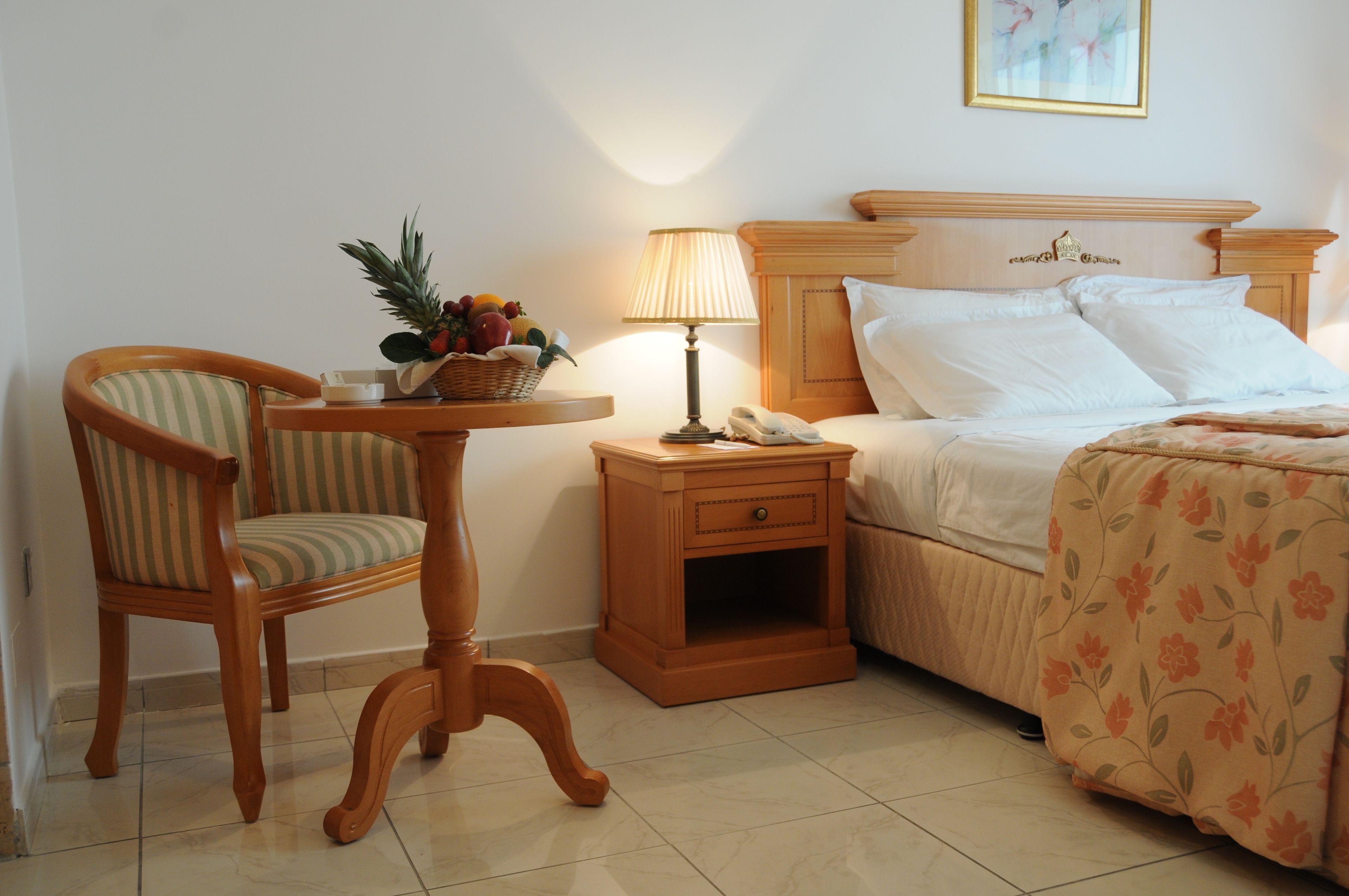 Une chambre d’hôtel avec un lit, une chaise, une table de chevet avec une lampe et une petite table sur laquelle se trouve un panier de fruits.