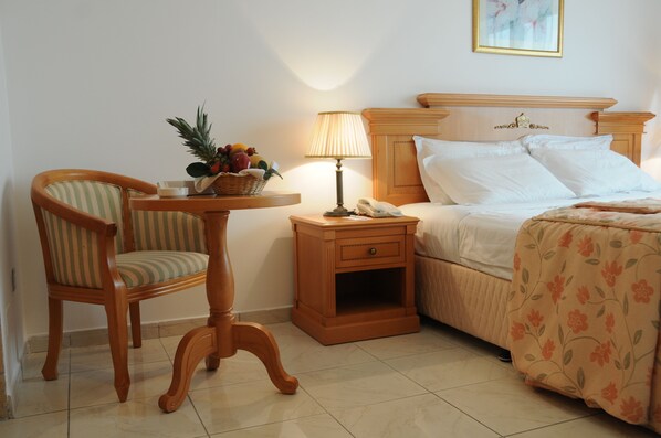 A hotel room with a bed, a chair, a nightstand with a lamp, and a small table with a fruit basket.