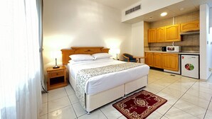 Habitación de hotel con cama, mesita de noche, lámpara y una pequeña kitchenette.