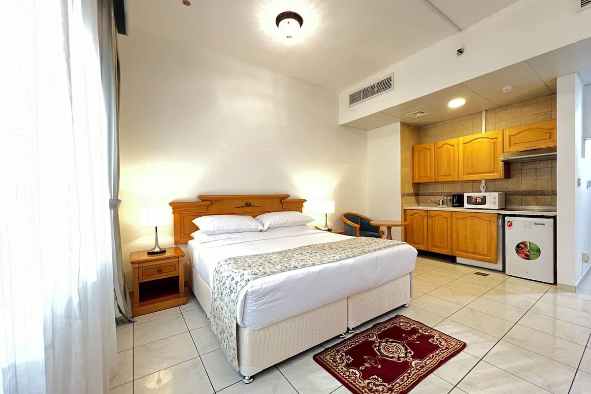 A hotel room with a bed, bedside table, lamp, and a small kitchenette.