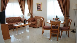 Una sala de estar con un sofá, una mesa de centro, un televisor, una lámpara, una mesa de comedor con sillas y un cuadro en la pared.