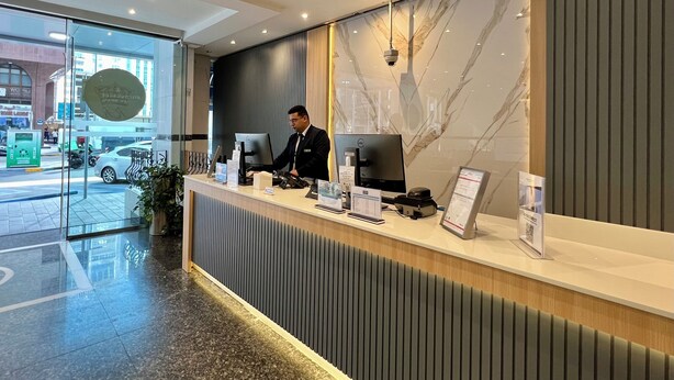 Un mostrador de recepción moderno con una recepcionista, una computadora y una pantalla digital.