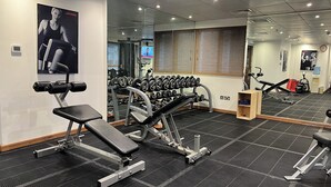 Un gimnasio con equipo de ejercicio, una banca, un estante de mancuernas y un espejo.