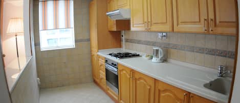 A kitchen with wooden cabinets, a stove, a sink, and a window with striped blinds.