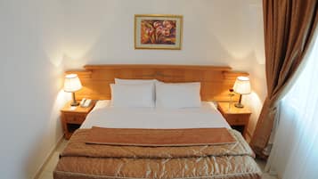 A neatly made bed with a headboard, two bedside lamps, a telephone, and a painting on the wall.