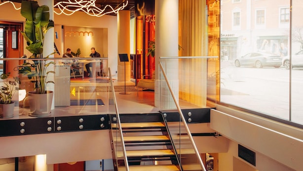 A modern hotel lobby with a staircase, potted plants, and a view of the street outside. - Scandic Go, Grensen 20 (Oslo)
