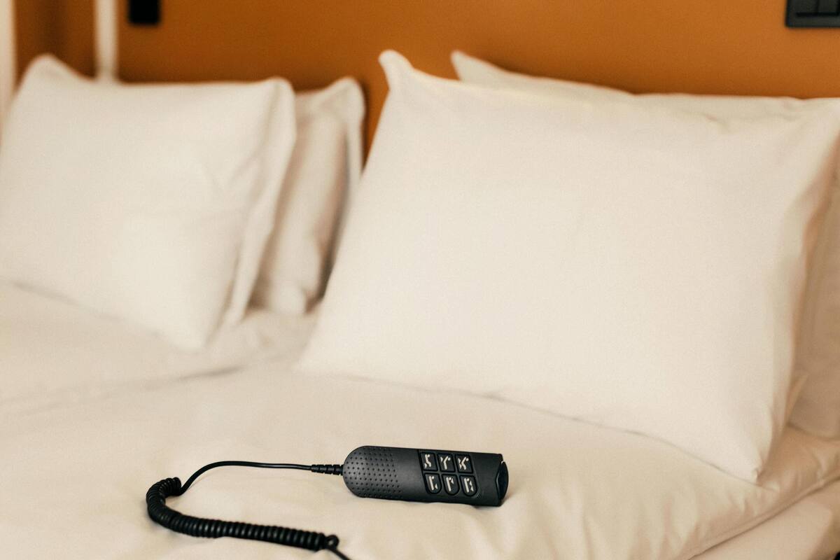 A bed with white pillows and a black remote control on it.