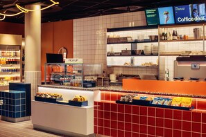 A coffee shop area with a pick-up counter, shelves with coffee and snacks, and a display of coffee-related items. - Scandic Go, Grensen 20 (Oslo)