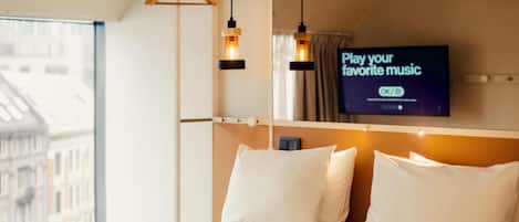 Habitación de hotel con cama, televisión montada en la pared y ventana con vista a edificios.