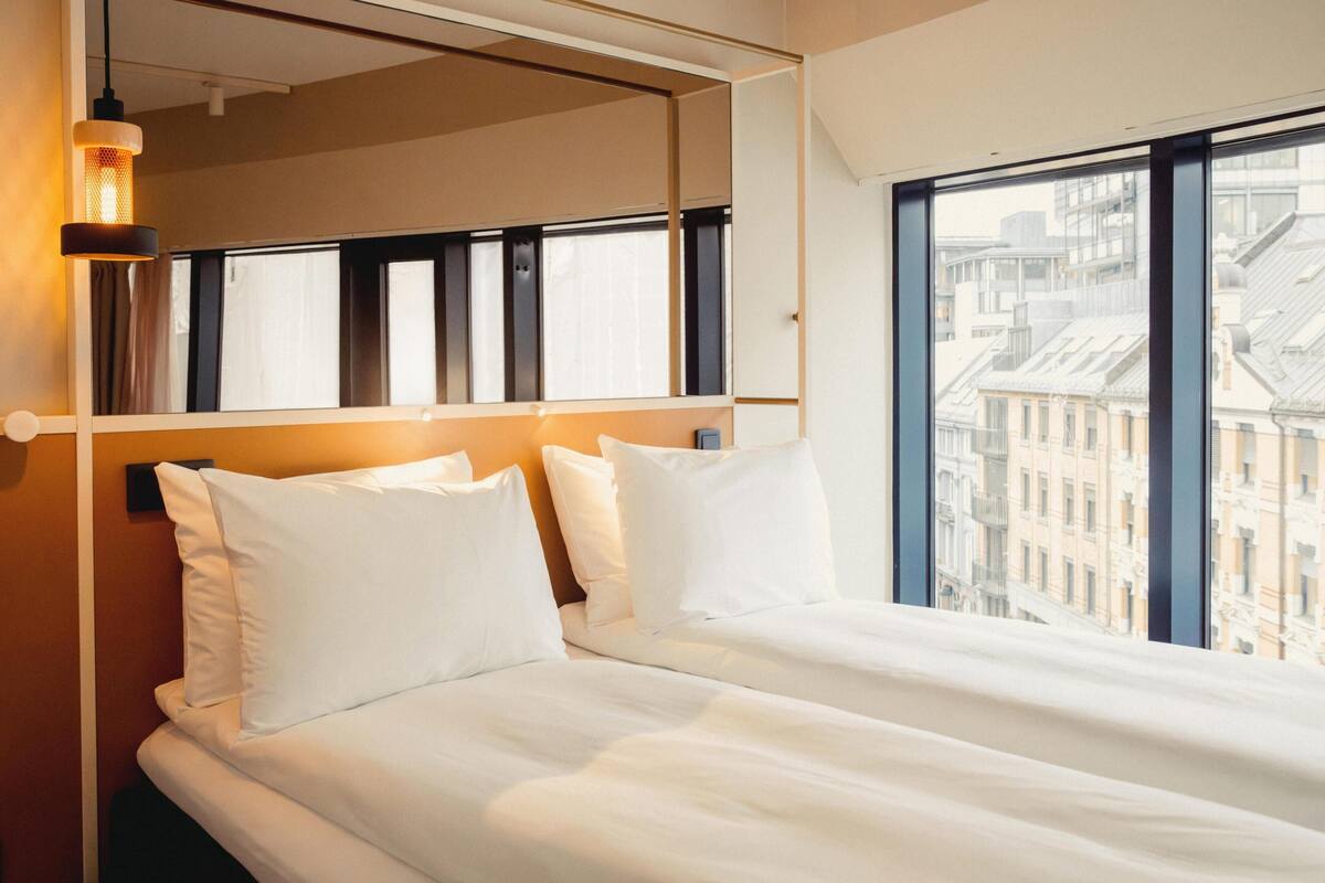 A hotel room with a large window, a bed with white linens, and a wall-mounted mirror.
