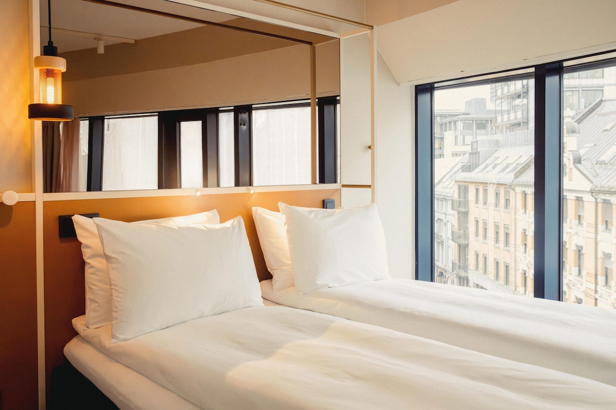 A hotel room with a large window, a bed with white linens, and a wall-mounted mirror.