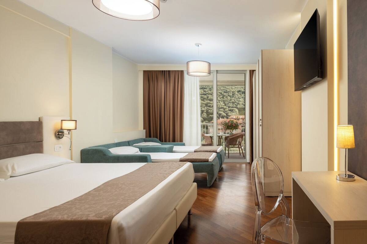 A hotel room with a bed, two sofas, a desk, a TV, and a balcony with a view.