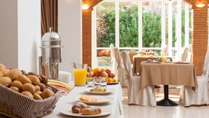 A breakfast buffet with bread, pastries, and fruit, set in a bright room with a view of greenery. - Hotel Savoy Palace - Tonelli Hotels (Riva del Garda)