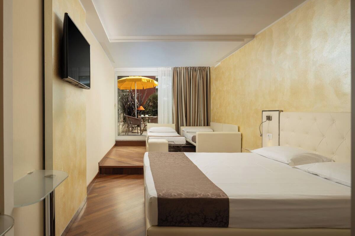 A hotel room with two beds, a TV, a balcony with an umbrella, and a small table.