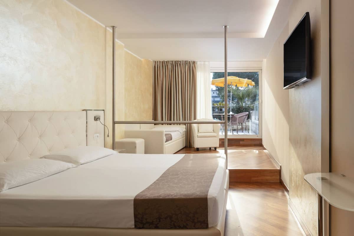 A modern hotel room with a large bed, a seating area with a table, and a TV mounted on the wall.