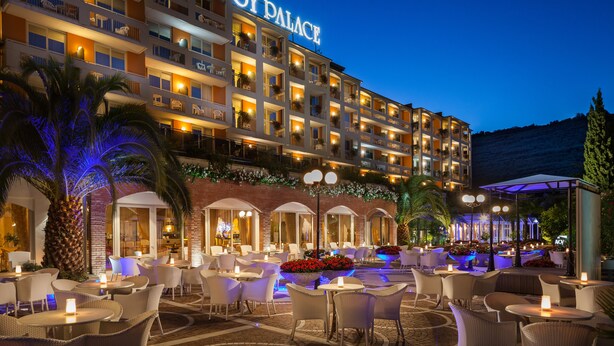A multi-story hotel with a well-lit exterior, outdoor seating area with tables and chairs, and a visible sign reading "HOTEL AVOY PALACE". - Hotel Savoy Palace - Tonelli Hotels (Riva del Garda)