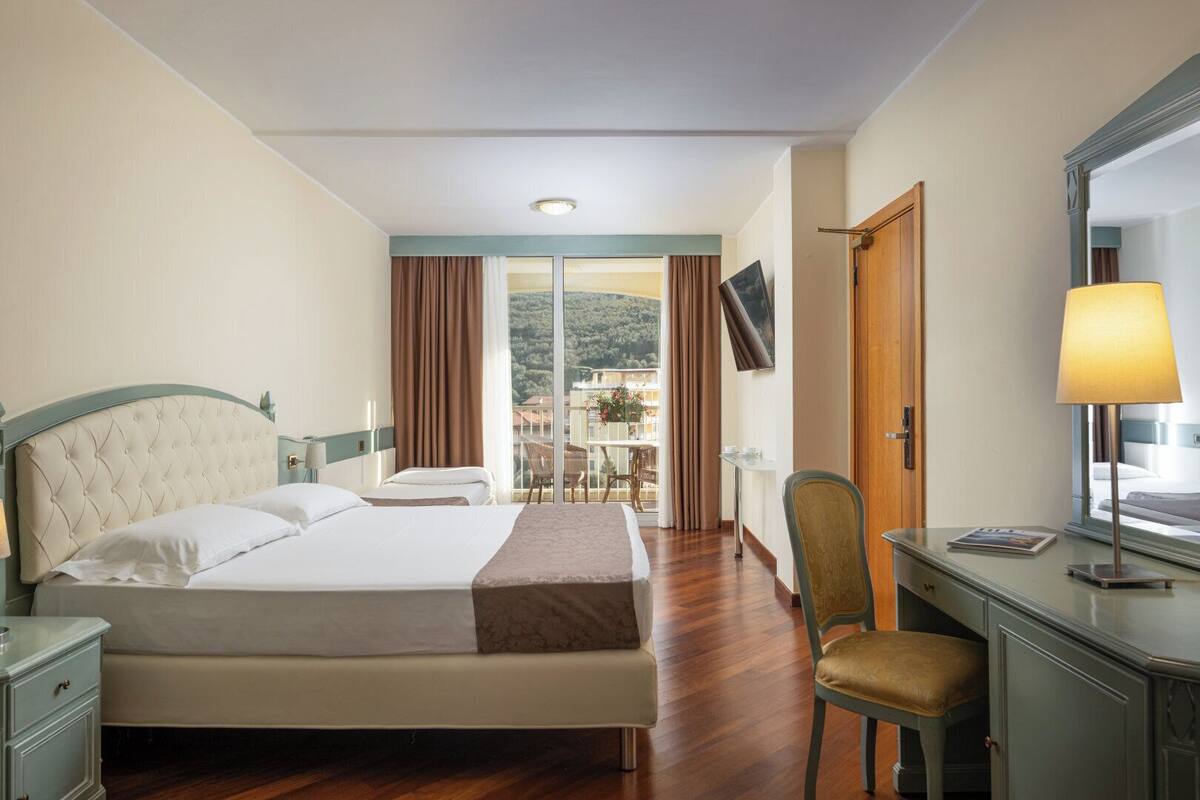 A hotel room with a bed, a desk, a chair, a TV, and a balcony with a view.