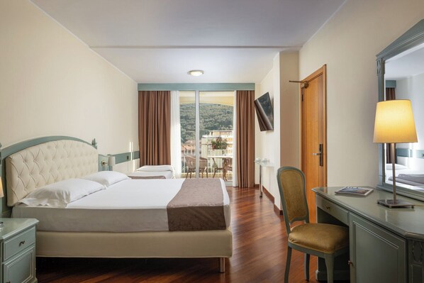 A hotel room with a bed, a desk, a chair, a TV, and a balcony with a view.