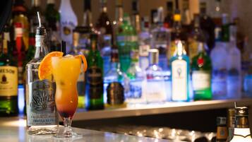 Eine Bar mit einer Auswahl an Spirituosenflaschen im Hintergrund und ein Cocktail mit Orangenscheibe auf der Theke.