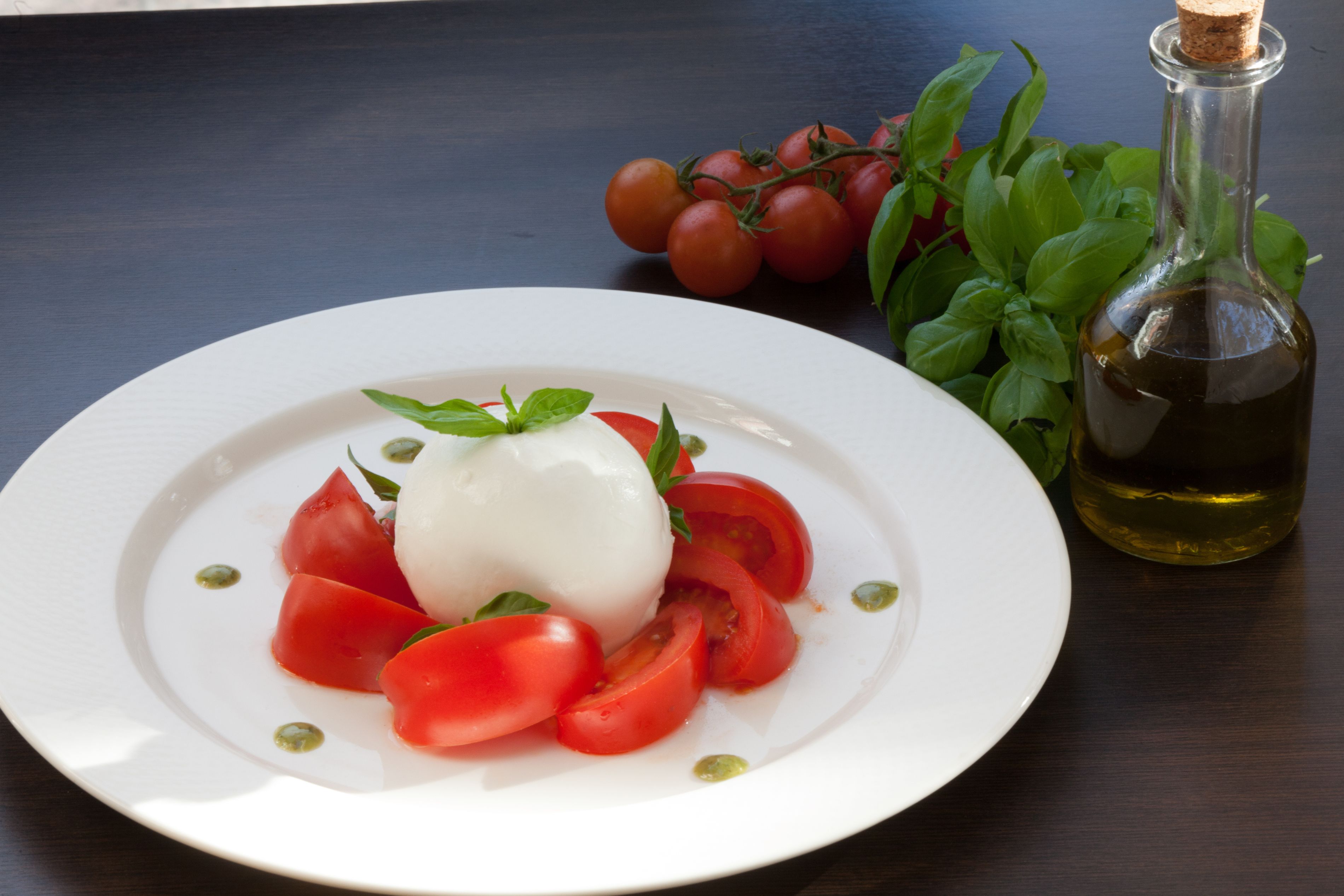 Ensalada Caprese con tomates, mozzarella y albahaca, acompañada de una botella de aceite de oliva.