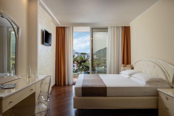 Habitación de hotel con cama, escritorio, silla, televisor y balcón con vistas a la ciudad.