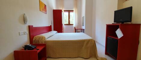 A hotel room with a bed, a desk, a chair, a TV on a stand, and a window with curtains.