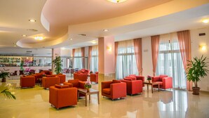 Een hotellobby met oranje zitplaatsen, een receptie en grote ramen voorzien van gordijnen.
