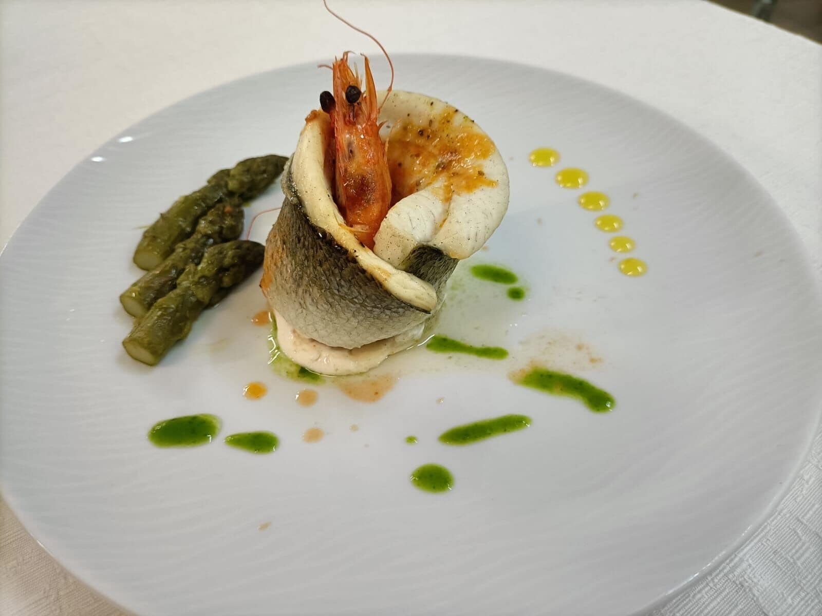 Un plato con mariscos, espárragos y salsa verde.