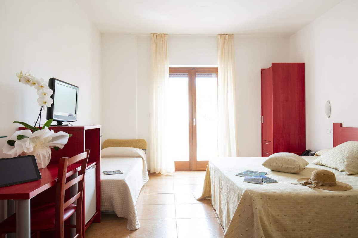 Une chambre d’hôtel équipée d’un bureau, de deux lits, d’une armoire et offrant une vue sur l’extérieur.