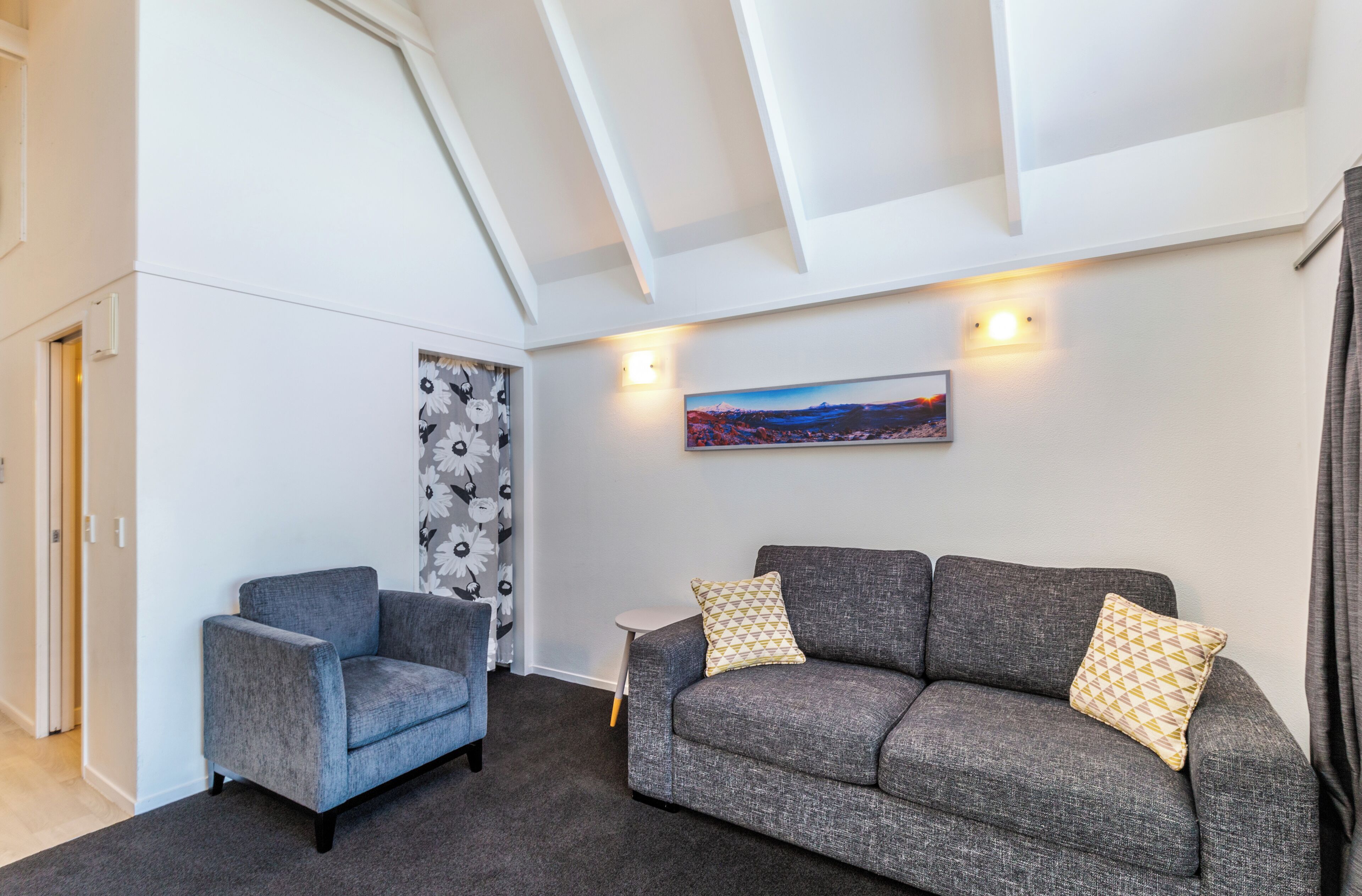 Una sala de estar moderna con un sofá y un sillón grises, una mesita auxiliar y un cuadro en la pared.