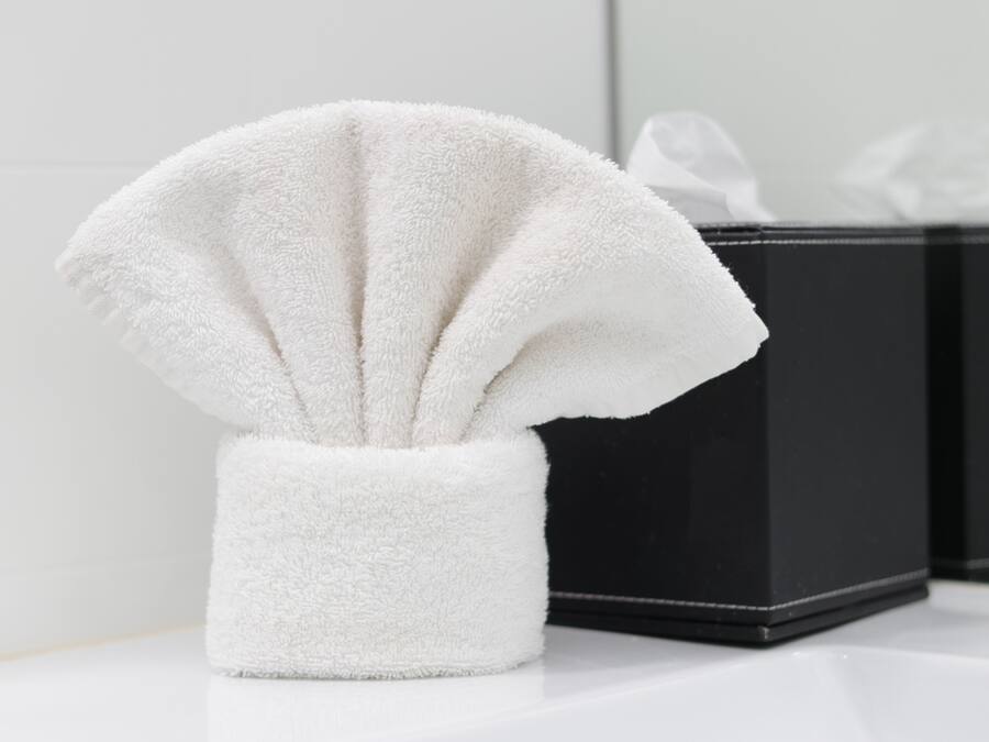 Een witte handdoek in een witte houder op een wit oppervlak, met een zwarte doos op de achtergrond.