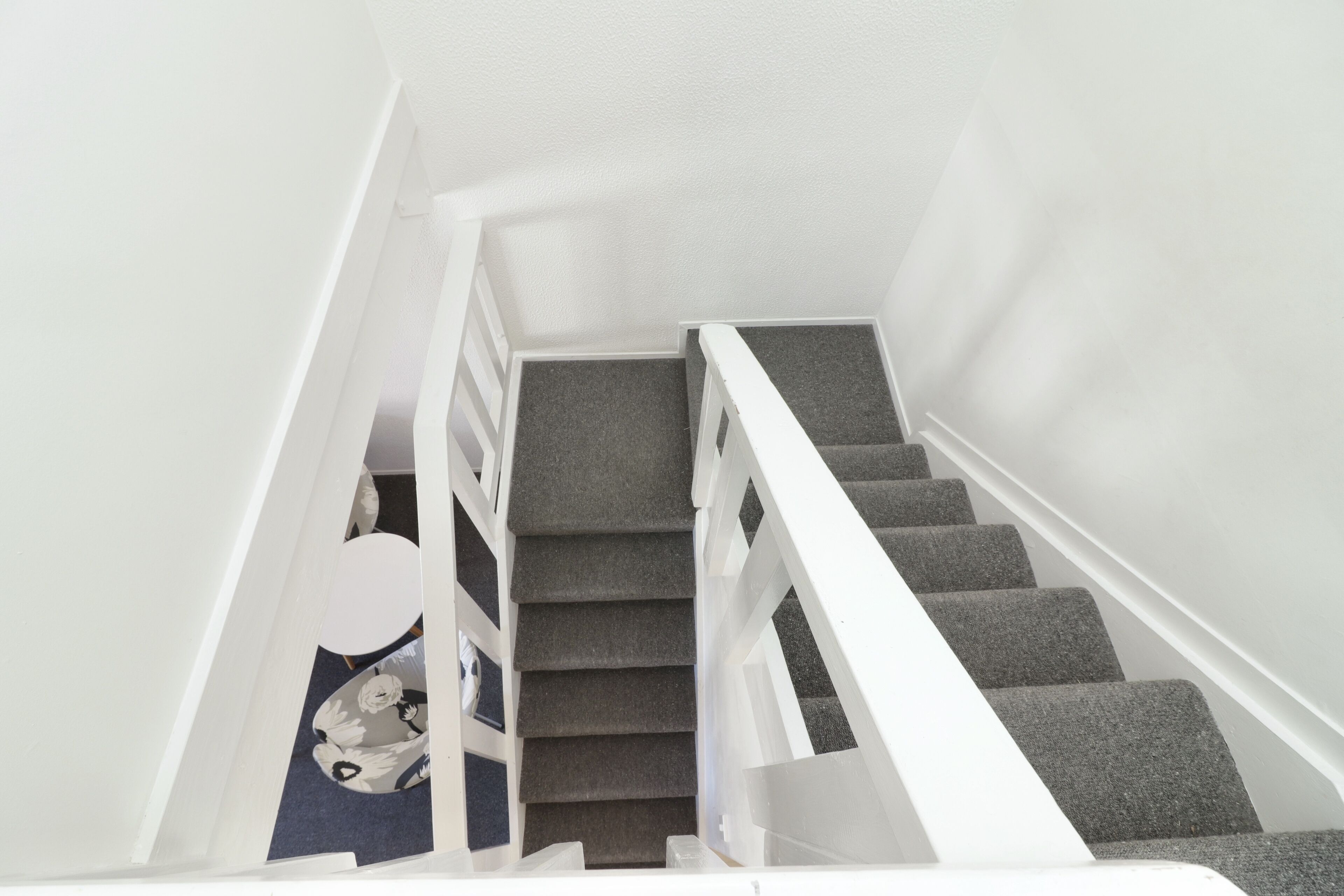 Una escalera con peldaños alfombrados de color gris y barandillas blancas.