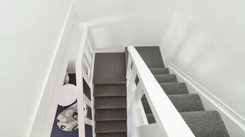 Una escalera con peldaños alfombrados de color gris y barandillas blancas.