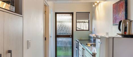 A modern kitchen with stainless steel appliances, a sliding glass door leading to a balcony, and a colorful abstract painting on the wall.