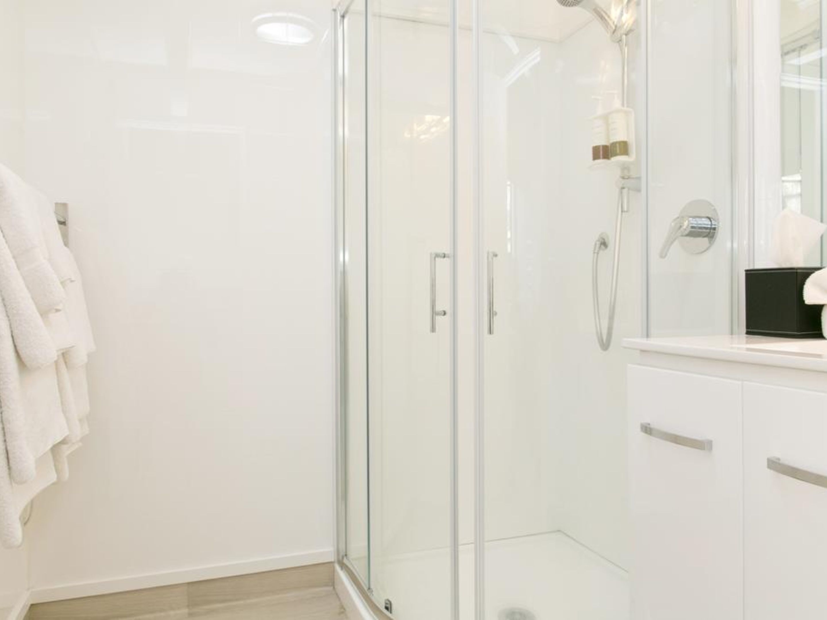 Un baño moderno con cabina de ducha de vidrio, un lavamanos blanco y un perchero para toallas.
