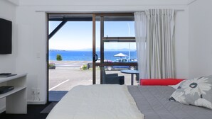 A hotel room with a bed, a desk, a chair, and a view of the sea. - Gables Lakefront Motel (Taupo)