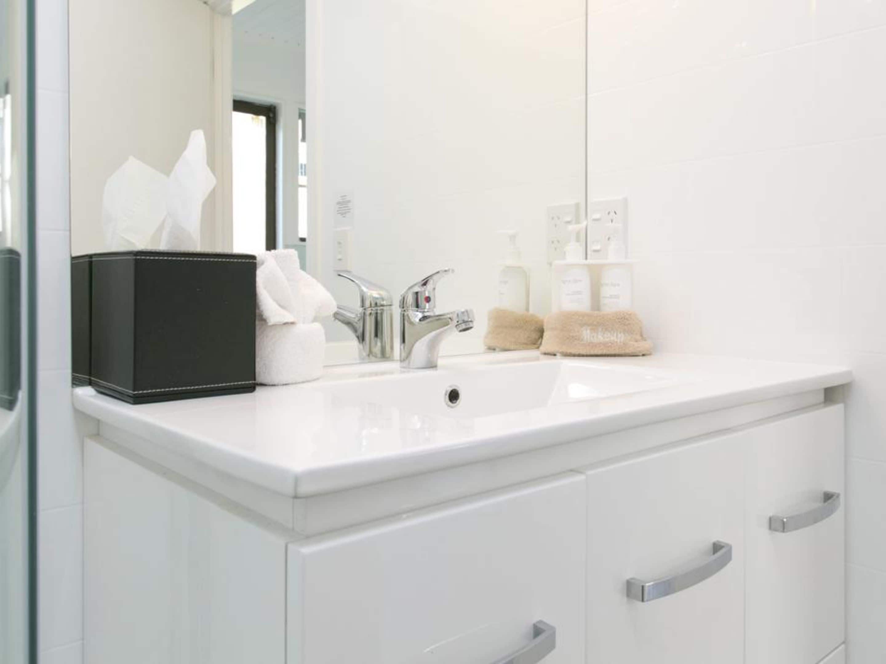 Une salle de bain moderne avec un lavabo blanc, deux robinets, un miroir et une boîte de rangement noire.