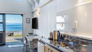 A modern kitchen with a large window overlooking the sea, a flat-screen TV mounted on the wall, and stainless steel appliances. - Gables Lakefront Motel (Taupo)
