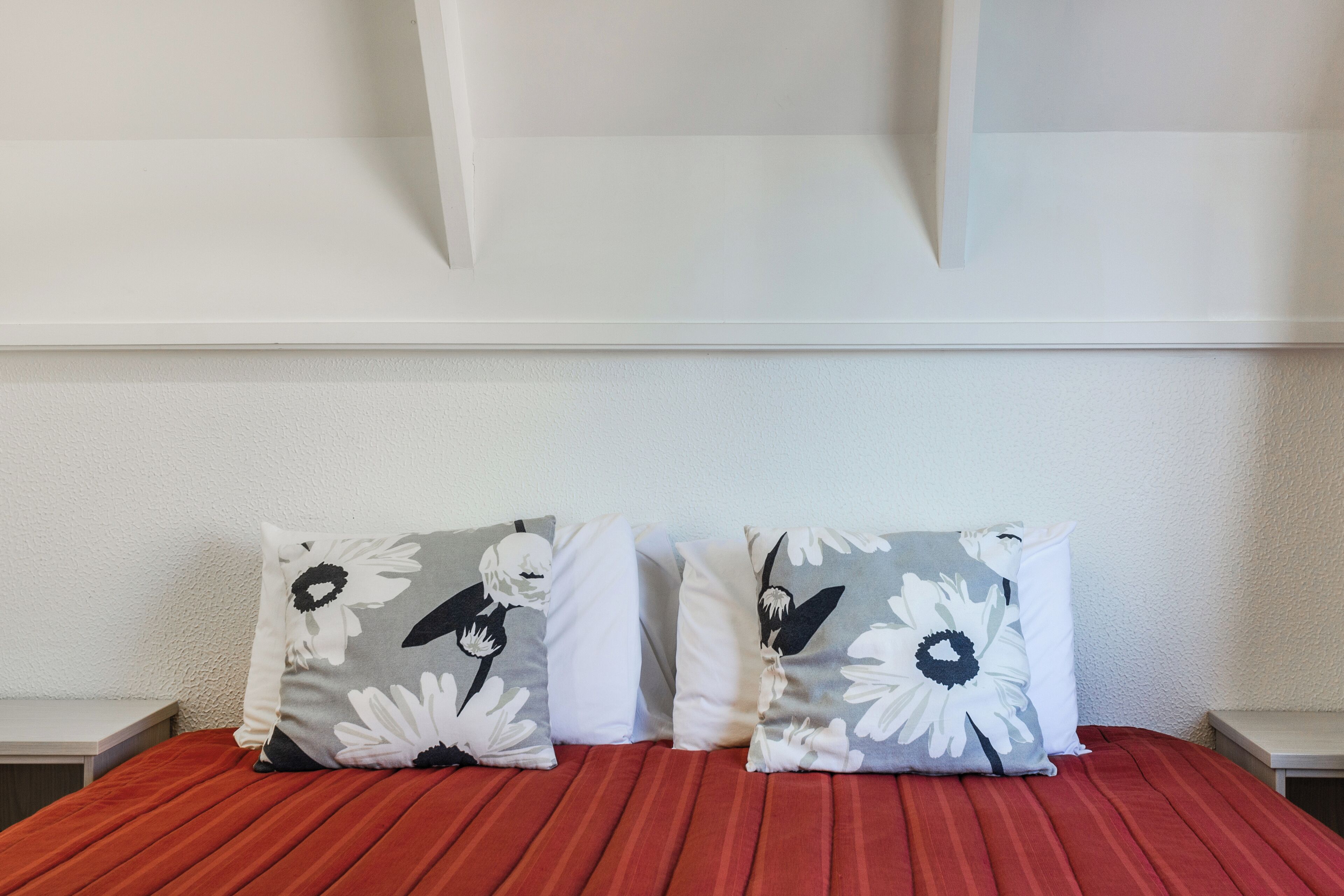 Ein Bett mit roter Bettdecke und zwei Kissen mit Blumenmuster.