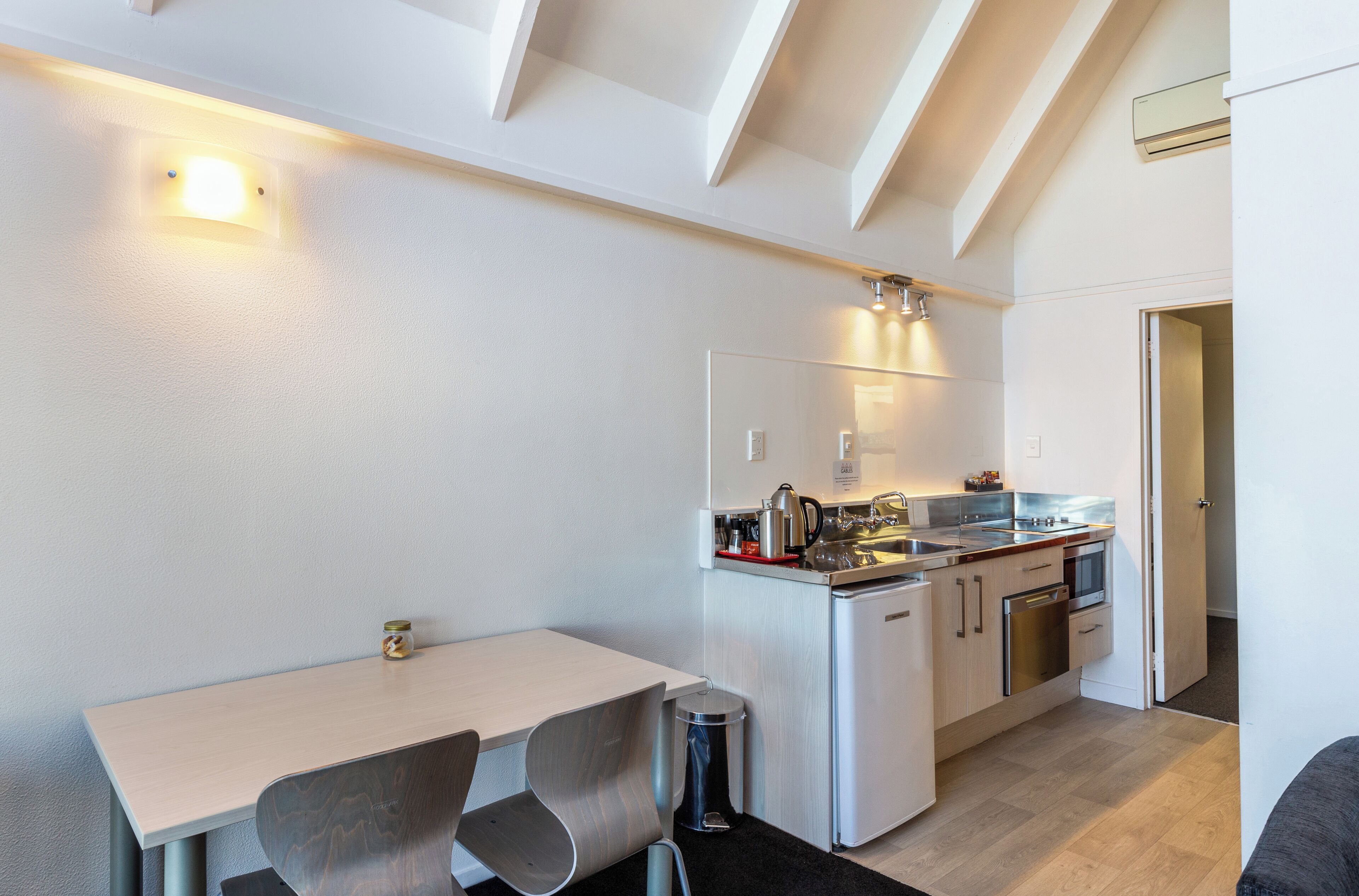 A compact kitchen with a dining area, featuring a white countertop, stainless steel appliances, and a modern design.