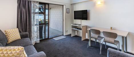 A modern room with a sofa, two chairs, a TV, and a sliding glass door leading to an outdoor area.