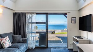 A modern room with a sofa, a TV, and a large sliding glass door leading to a balcony with a view of the sea. - Gables Lakefront Motel (Taupo)