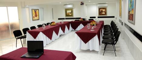 A conference room with long tables, chairs, a laptop, and paintings on the walls.