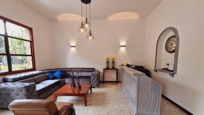A modern living room with a sectional sofa, a coffee table, a small armchair, a TV stand, and a decorative mirror. - Hotel Karlo (Cali)