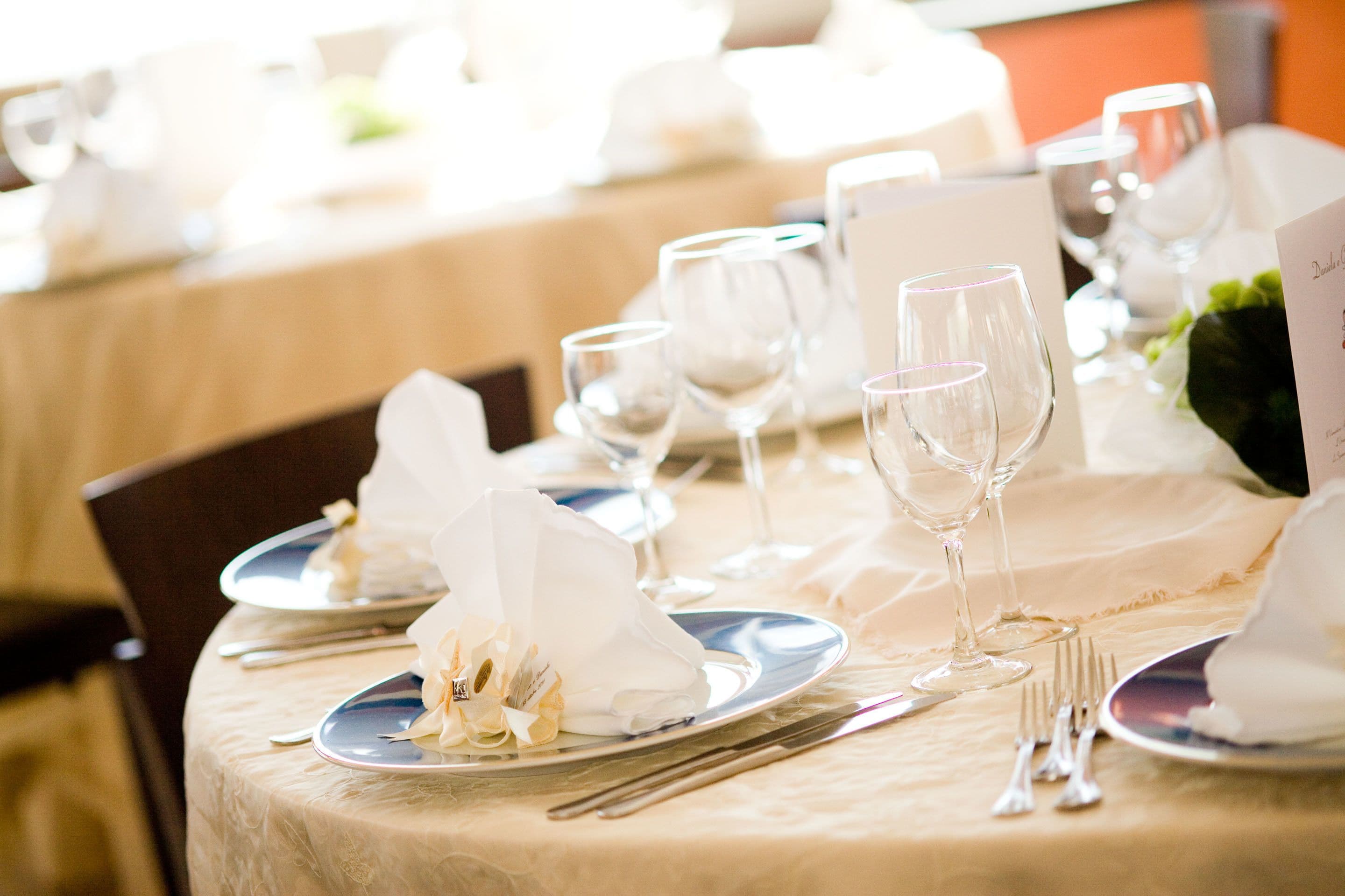 Una mesa de comedor redonda con mantel blanco, dispuesta con platos, vasos y cubiertos.
