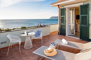 A balcony with a view of the sea, a table with chairs, and a lounge chair with a hat and towel. - Hotel Savoia (Alassio)