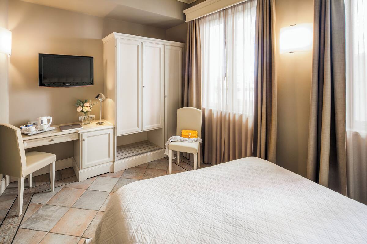 A hotel room with a bed, a desk with a chair, a television, and a wardrobe.