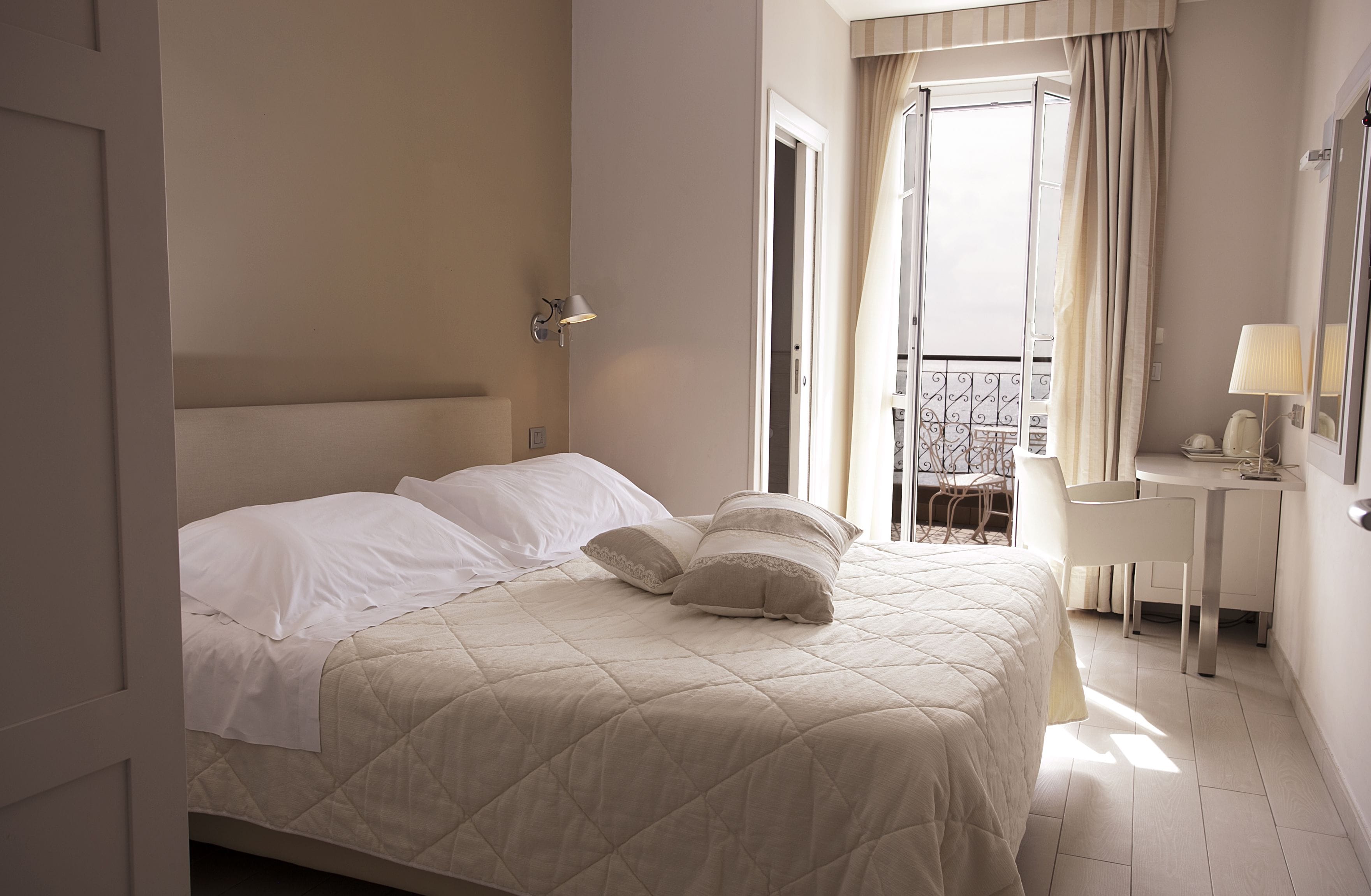 A hotel room with a bed, a desk, and a balcony with curtains.